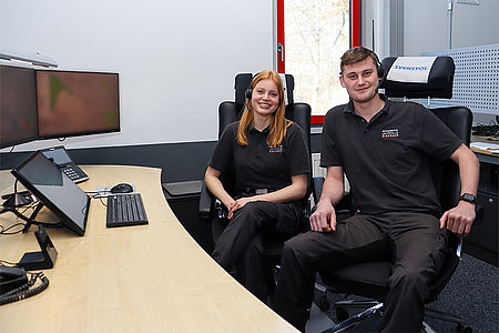 Ein junger Mann und eine junge Frau der Rettungsleitstelle mit Headsets lächeln in die Kamera.