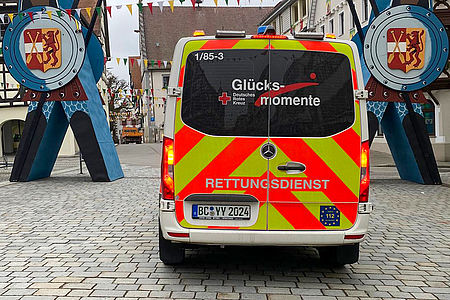 Ein Rettungswagen mit der Aufschrift "Glücksmomente" steht in einer Fußgängerzone.