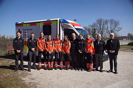 Neue Azubis und Mitarbeiter der DRK stehen vor einem Rettungswagen.