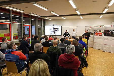 Eine größere Gruppe von Menschen hört einem Vortrag zu.