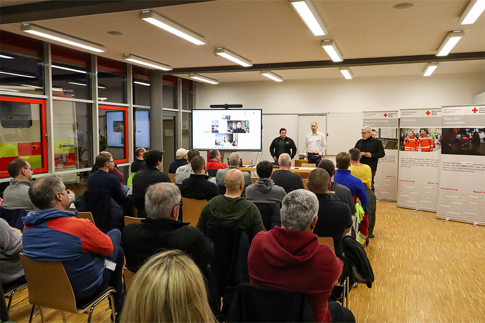 Eine größere Gruppe von Menschen hört einem Vortrag zu.