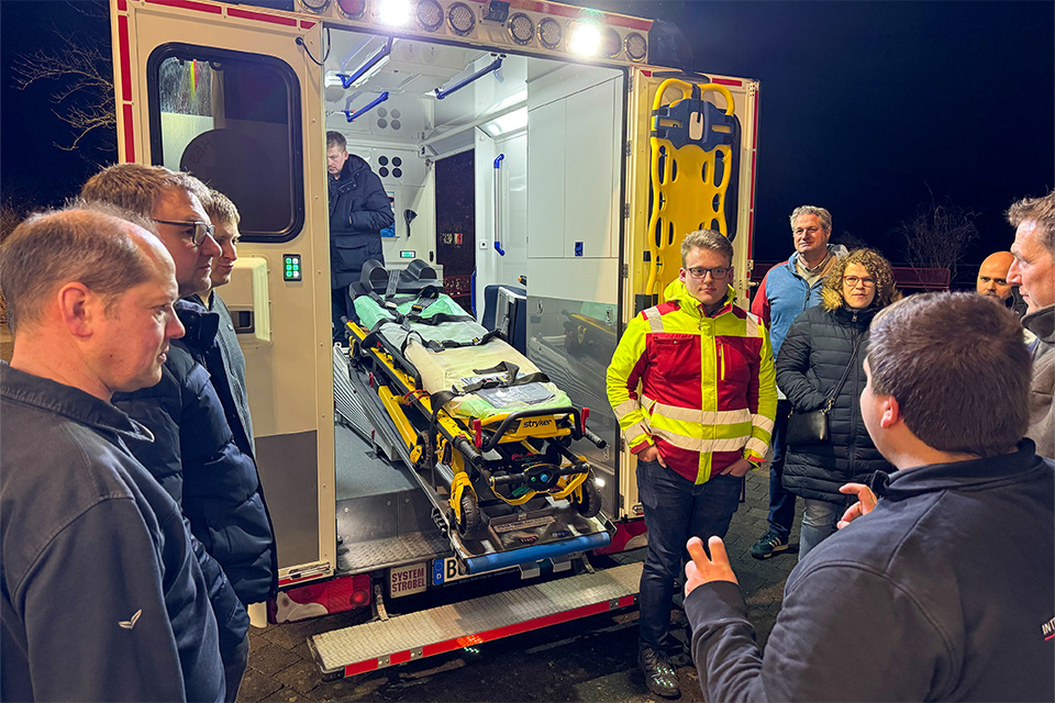 Einige Menschen stehen zusammen hinter einem Rettungswagen, dessen Tür geöffnet ist.
