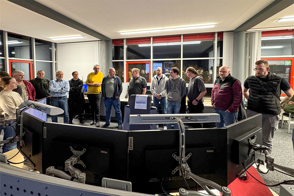 Einige Menschen stehen in einer Integrierten Leitstelle. Sie schauen gemeinsam viele Monitore an.