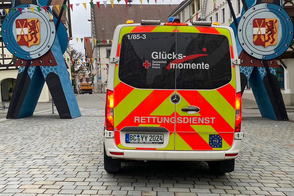 Ein Rettungswagen mit der Aufschrift "Glücksmomente" steht in einer Fußgängerzone.