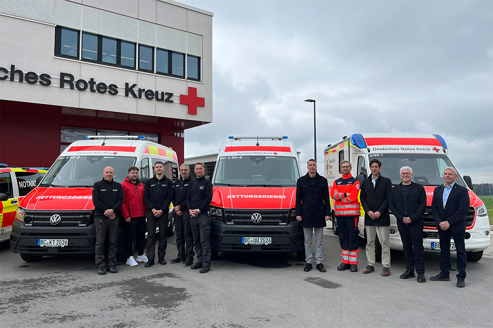 Mehrere Personen stehen vor drei Einsatzfahrzeugen beim DRK