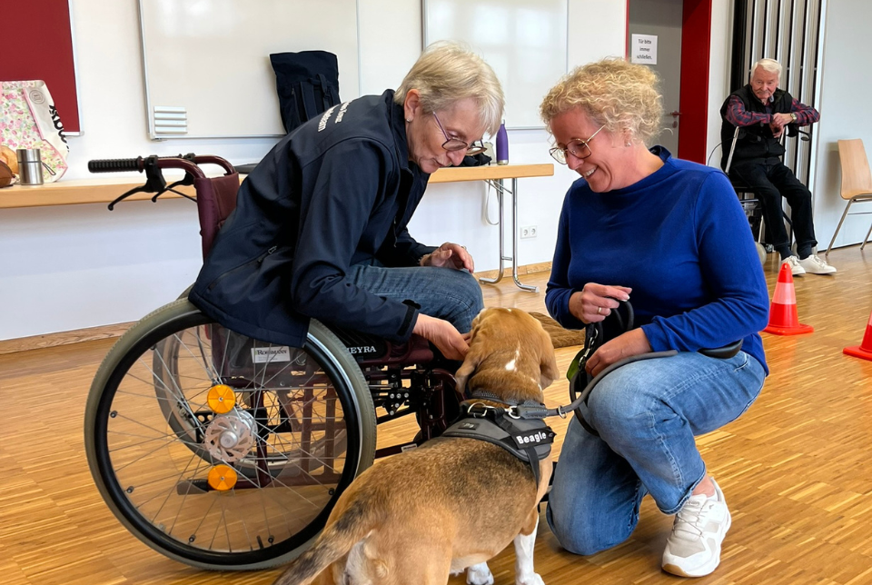 Therapiehunde Zwei Frauen, eine sitzt im Rollstuhl, bei ihnen ist ein Hund